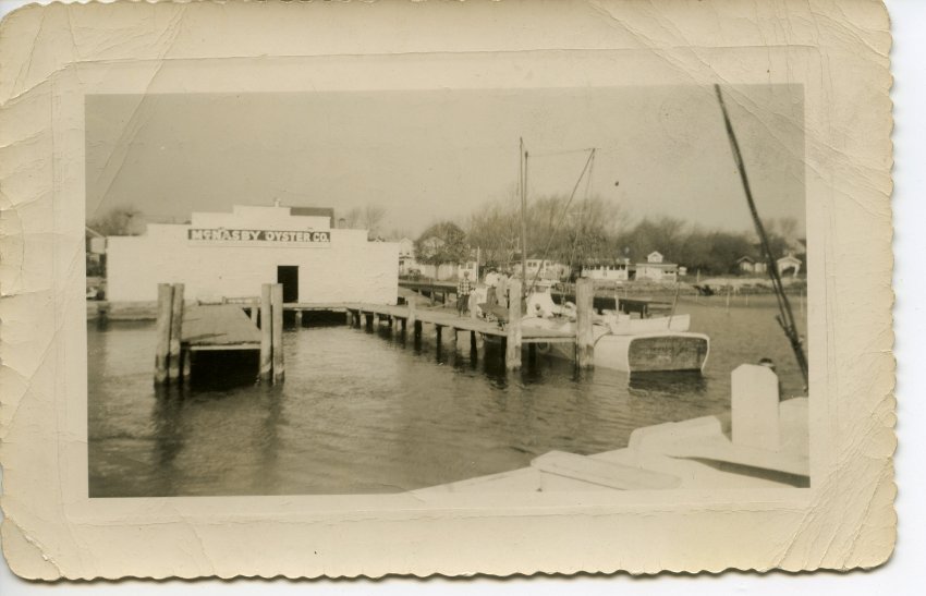 A view of McNasby's Oyster Co. on Second Street, taken from the water. A boat is docked and is unloading its catch.