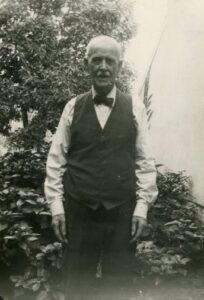 Photograph of William McNasby Sr., founder of the McNasby Oyster Co. business. He is dressed formally and is standing among trees and vegetation.